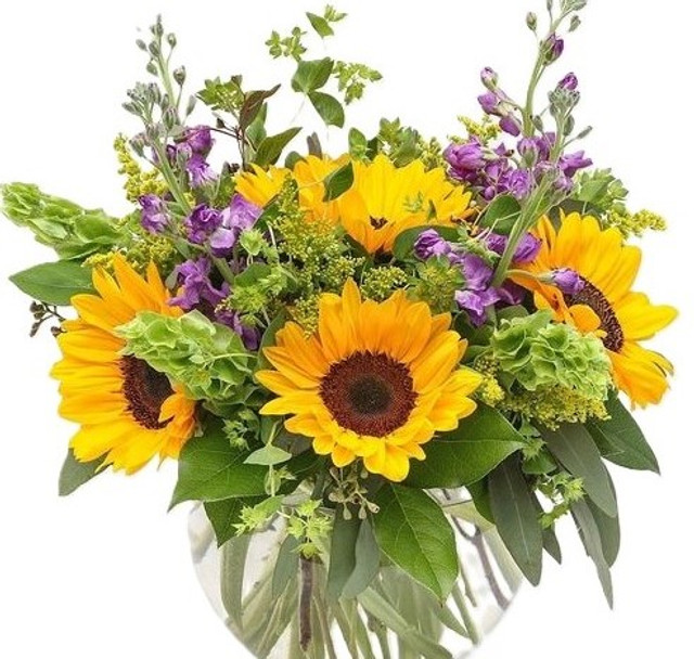 Cheerful arrangement of sunflowers, purple flowers, and greenery in a clear vase for a vibrant display.