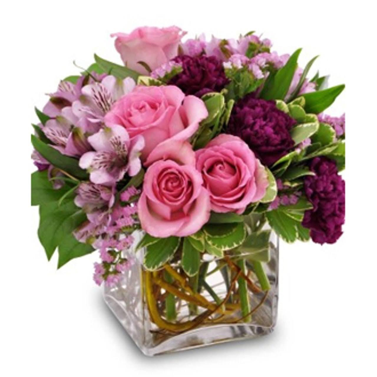 Pink spray roses with purple spring flowers and green leaves in a clear glass square vase.