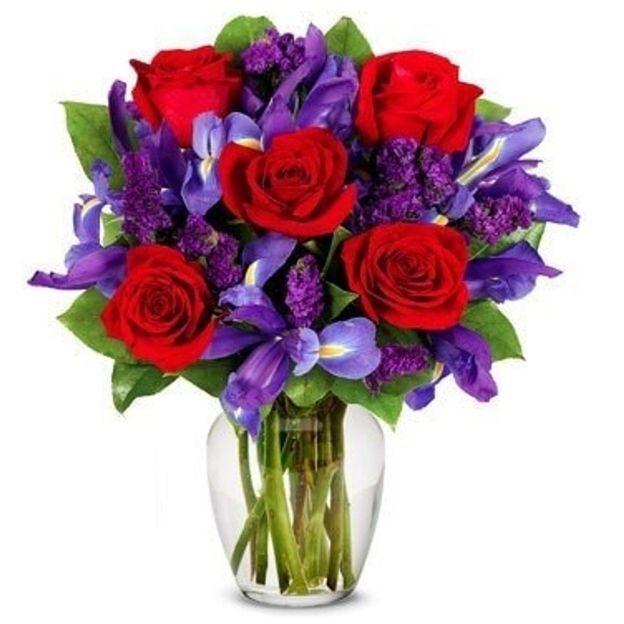 Clear vase holding a bouquet of red roses, purple irises, and violet filler flowers with lush green leaves.