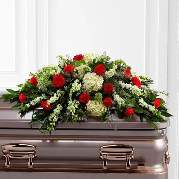 Elegant casket spray featuring red roses and white flowers with lush green leaves, displayed in a memorial setting.