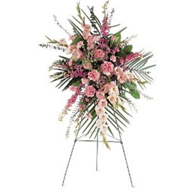 Standing funeral spray with pink carnations, gladiolus, and greenery arranged on a metal easel.