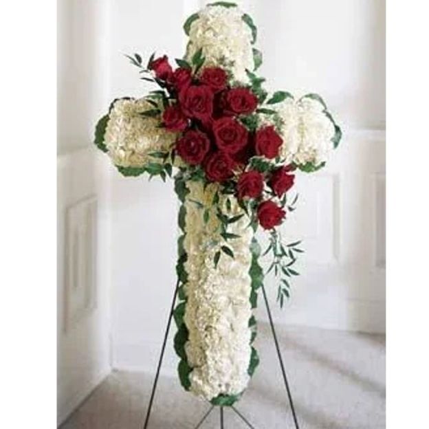 Standing floral cross featuring white blooms and red roses, symbolizing love and remembrance at a memorial service.