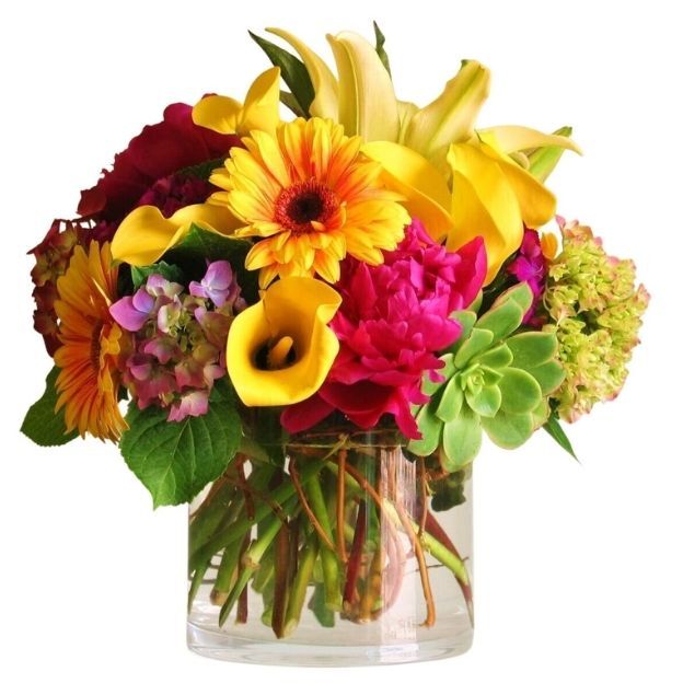 Vibrant bouquet of yellow, pink, red, and green flowers in a round glass vase with visible stems.