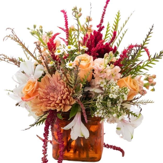 Peach roses, white alstroemeria, and mum with burgundy amaranthus and greenery in an amber glass cube vase.
