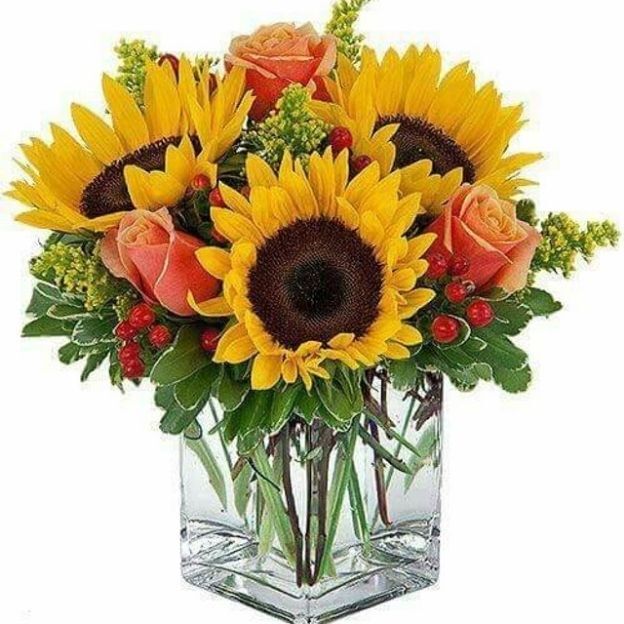 Cheerful floral arrangement featuring sunflowers, orange roses, red berries, and green leaves in a glass vase.