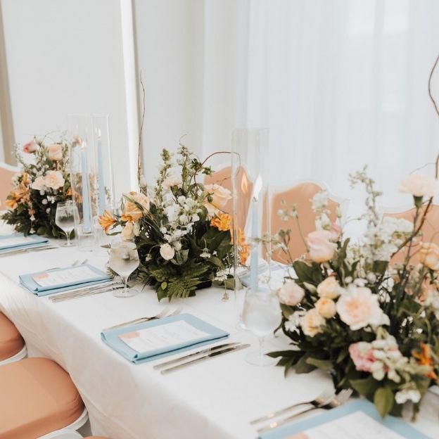 Elegant wedding reception table with peach chairs, pastel floral centerpieces, and blue-accented place settings.