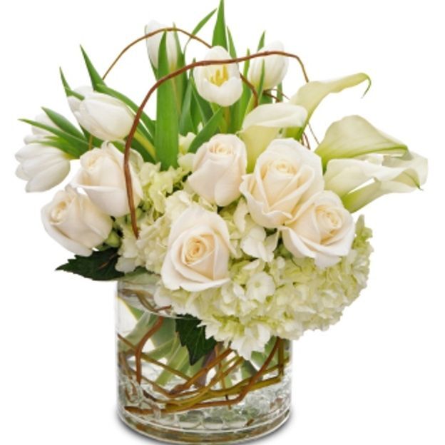 Elegant white floral arrangement featuring roses, tulips, calla lilies, and hydrangeas in a glass vase.