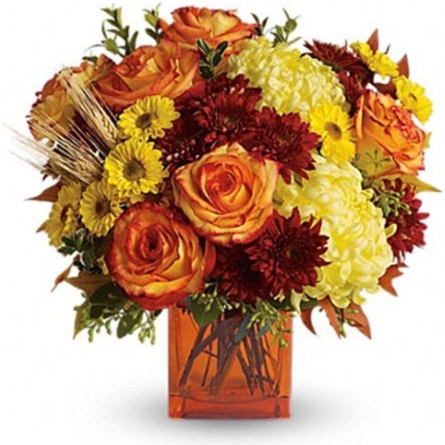 Fall mix of orange roses, yellow button mums, cream mums, red chrysanthemums, and greenery in an orange square vase.