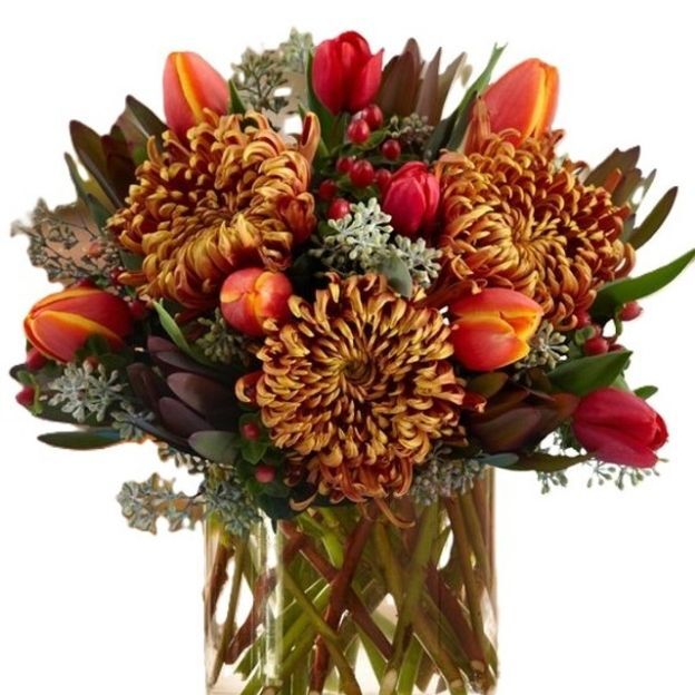 Autumn bouquet with bronze spider mums, red-orange tulips, hypericum berries, and greenery in a clear square vase.